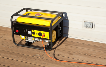 A yellow and black generator is sitting on a wooden deck next to a wall.