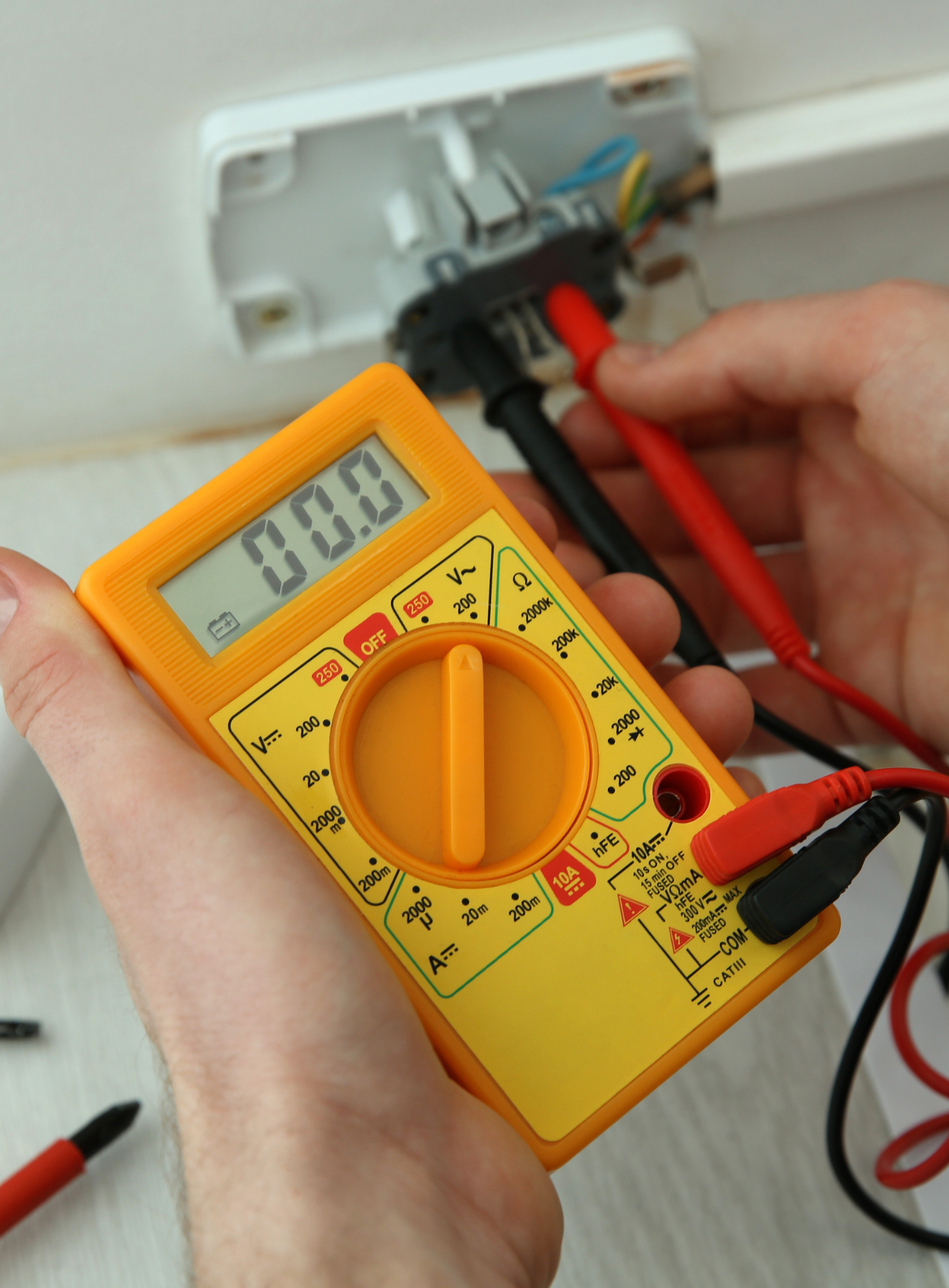 A person is using a digital multimeter with a display that reads 0.00