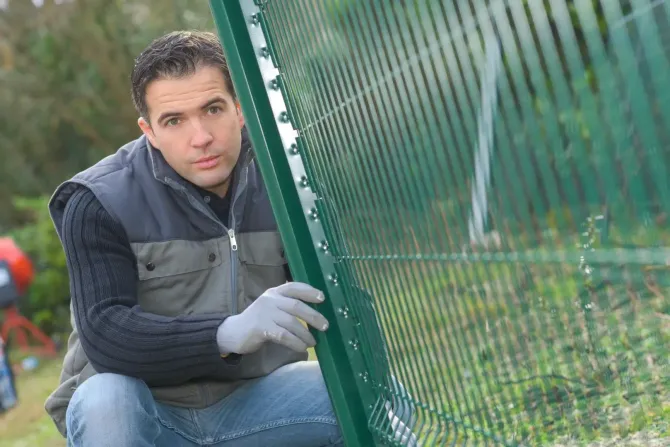 Worker installing green wire mesh security fencing.