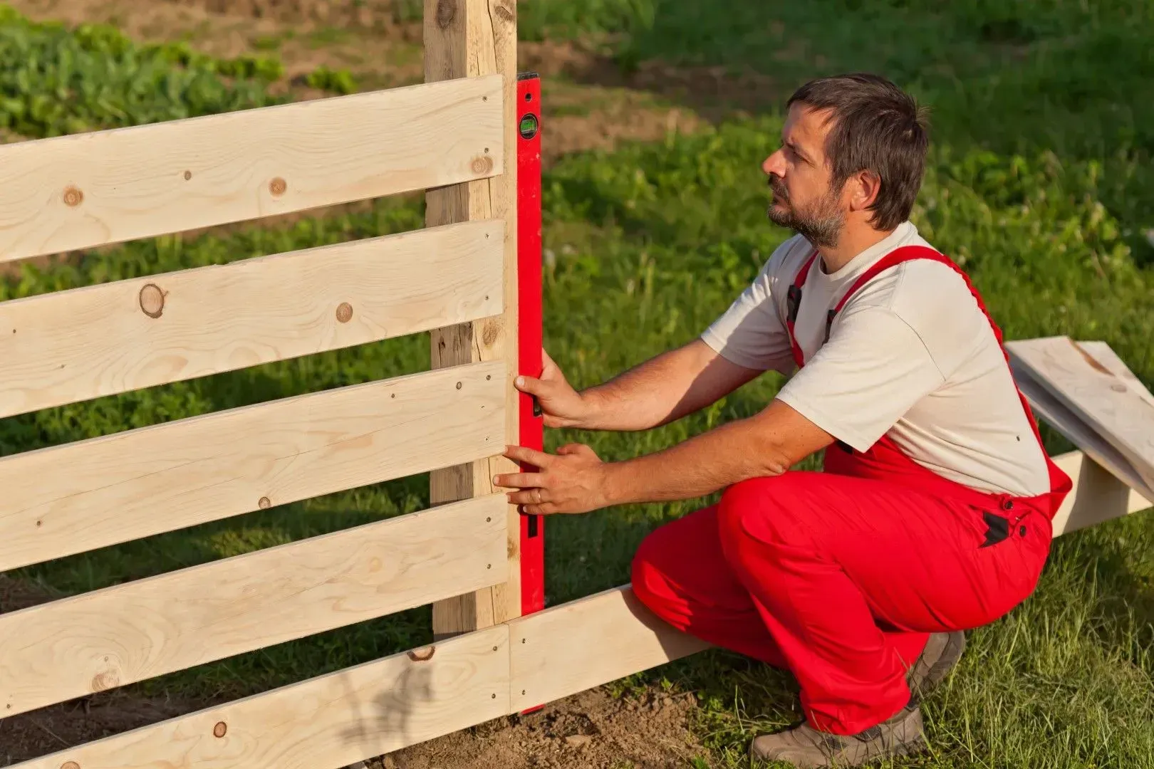 Worker leveling a new wooden garden fence.
