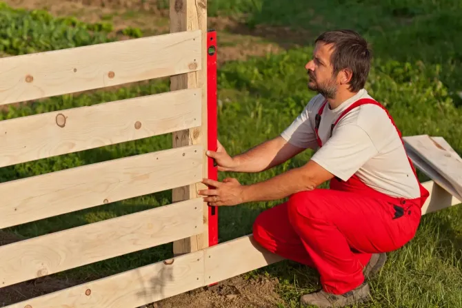 Worker leveling a new wooden garden fence.
