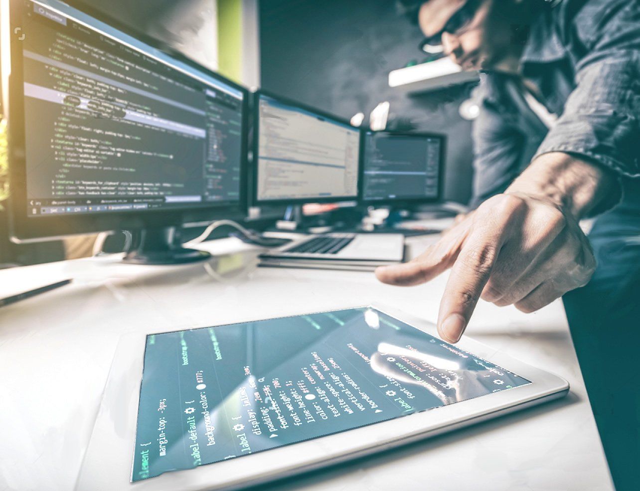 A man is using a tablet computer in front of a computer screen.