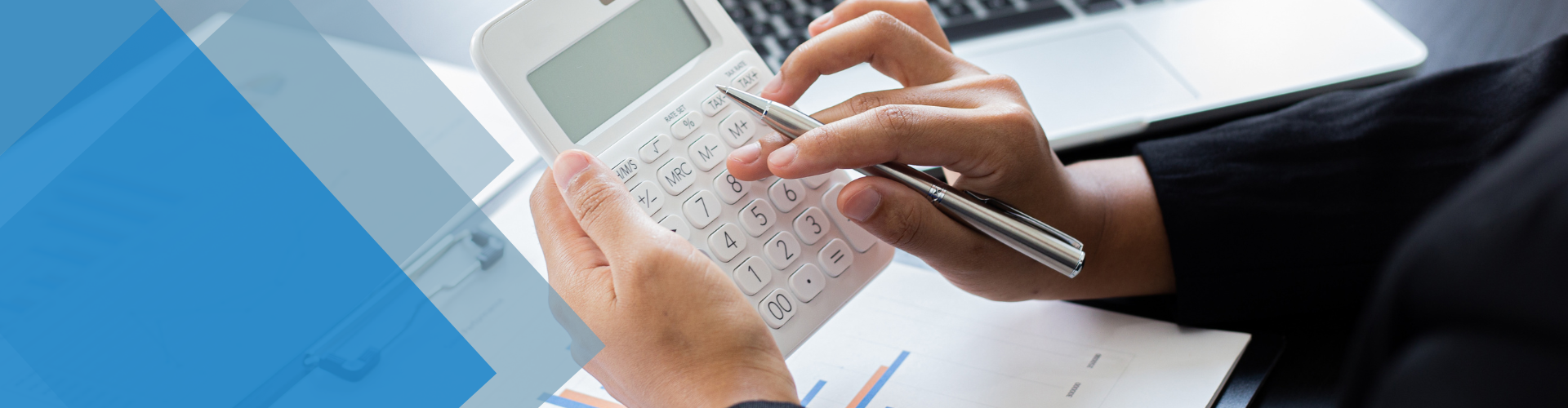 Person calculating with a calculator at a desk with a laptop; hands visible, indoors, soft lighting.