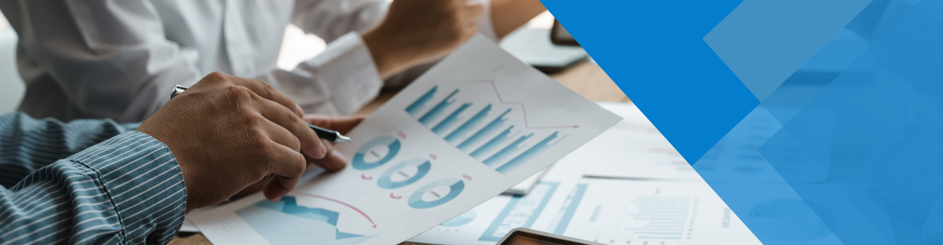 Hands pointing at a financial chart during a business meeting. Blue graphic element in the background.