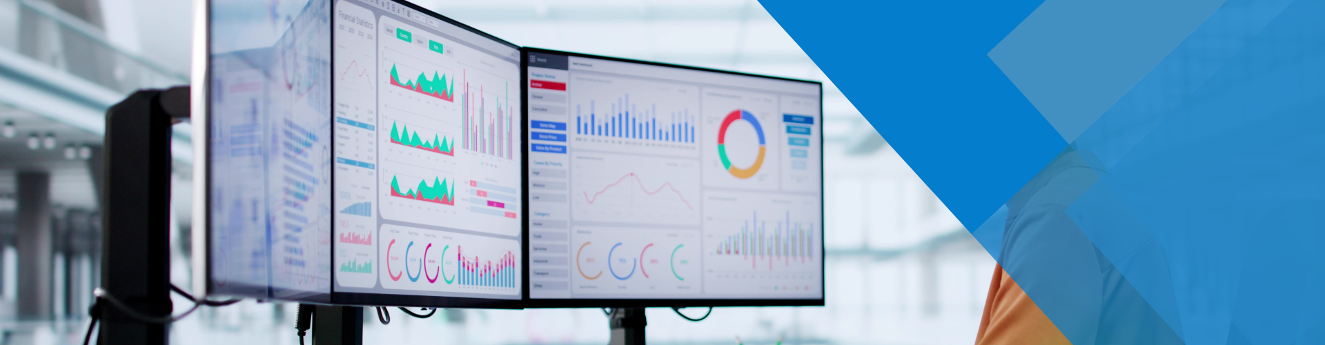 Three computer monitors displaying charts and graphs, in an office setting. A blue geometric design is in the right corner.