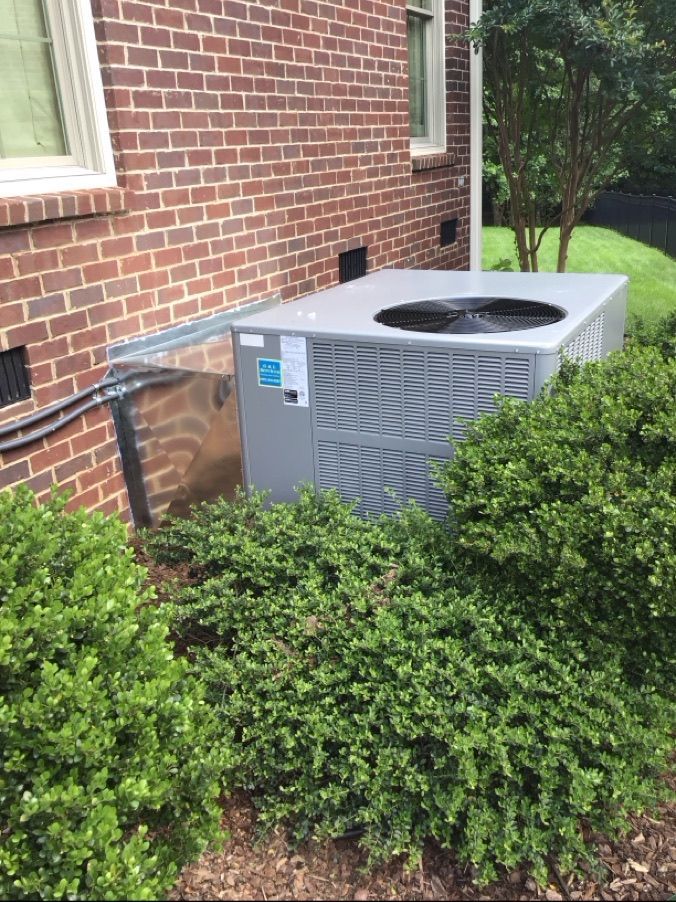 A large air conditioner is sitting on the side of a brick house.