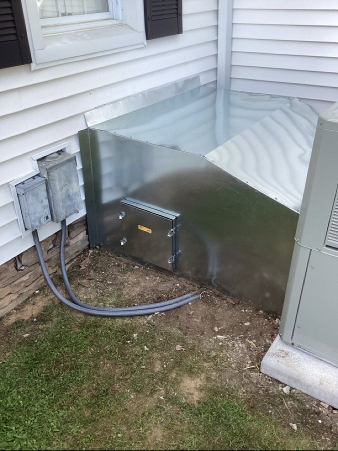 Metal utility enclosure and electrical boxes beside a house foundation, with conduit on the ground.