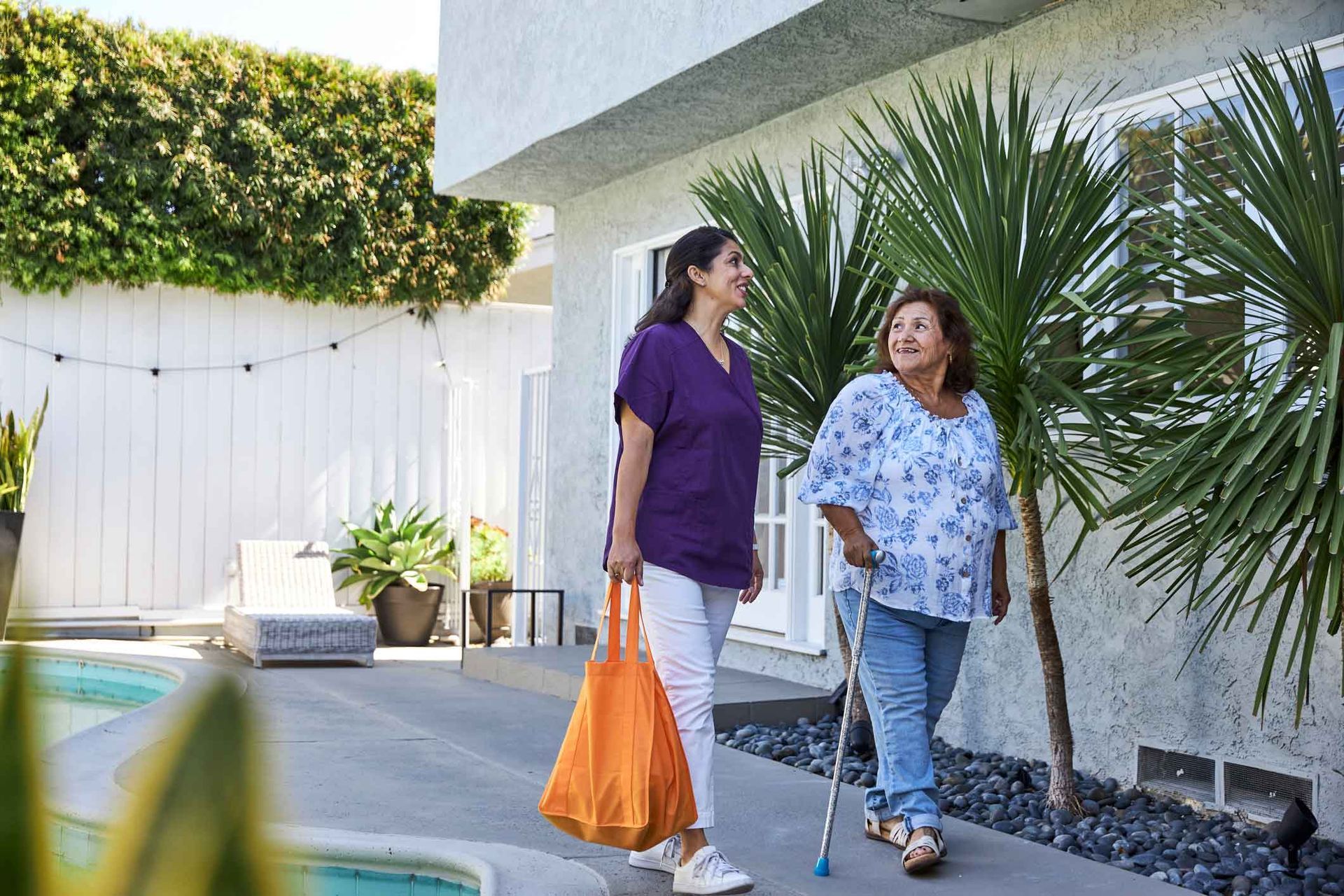 A nurse is walking with an elderly woman with a cane.