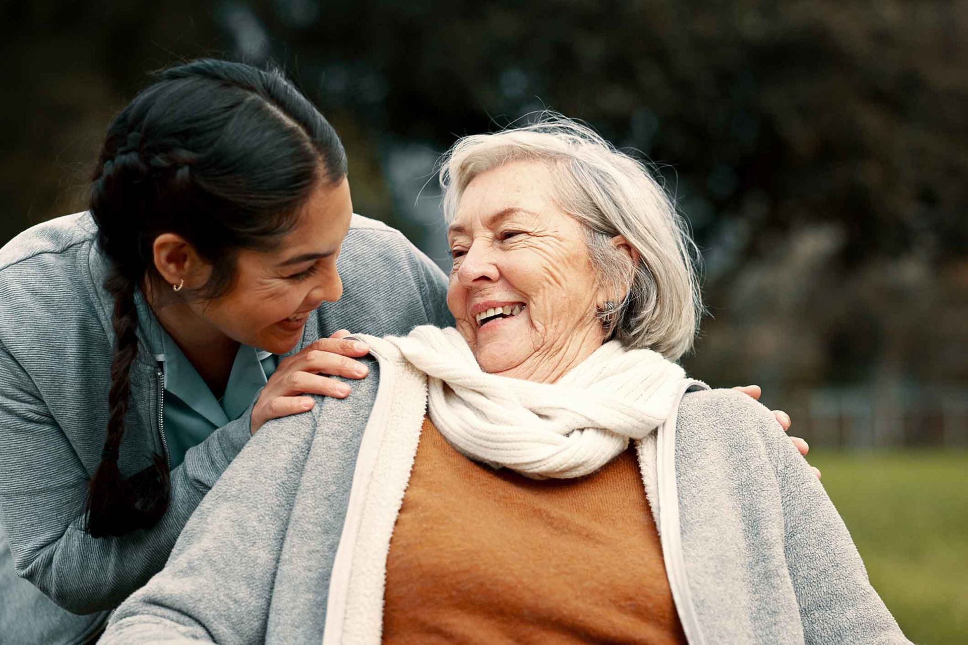 A young woman is hugging an older woman in a wheelchair.