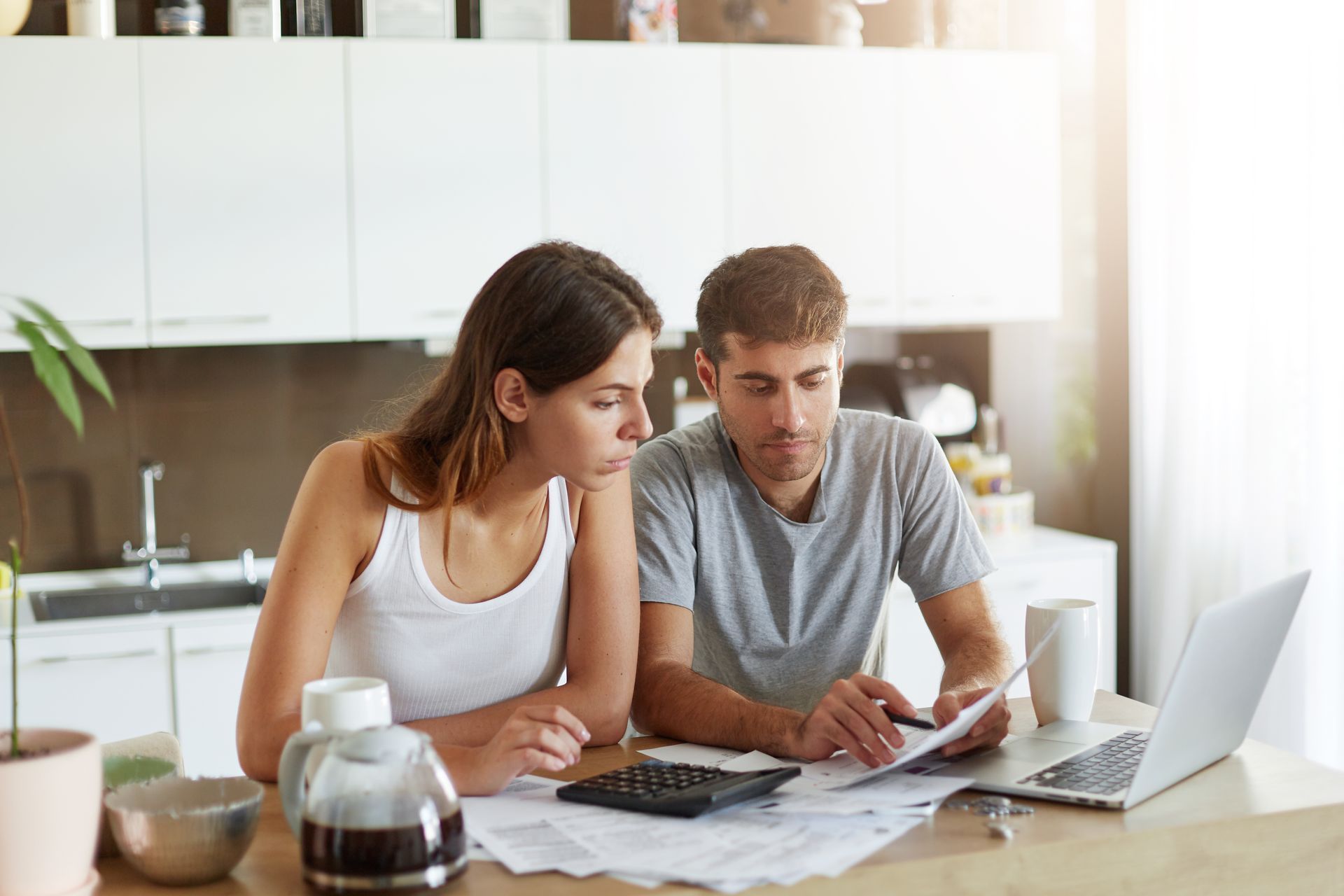 Two people reviewing papers at a kitchen table with a laptop and coffee pot nearby