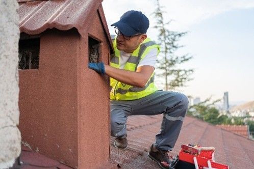A worker inspecting or repairing a chimney on a rooftop
