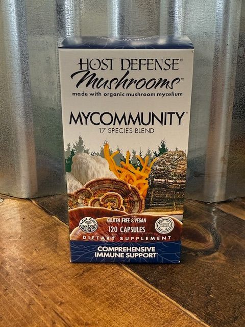 Box of Host Defense MyCommunity mushrooms supplement with 17 species blend, on wood and metal backdrop.