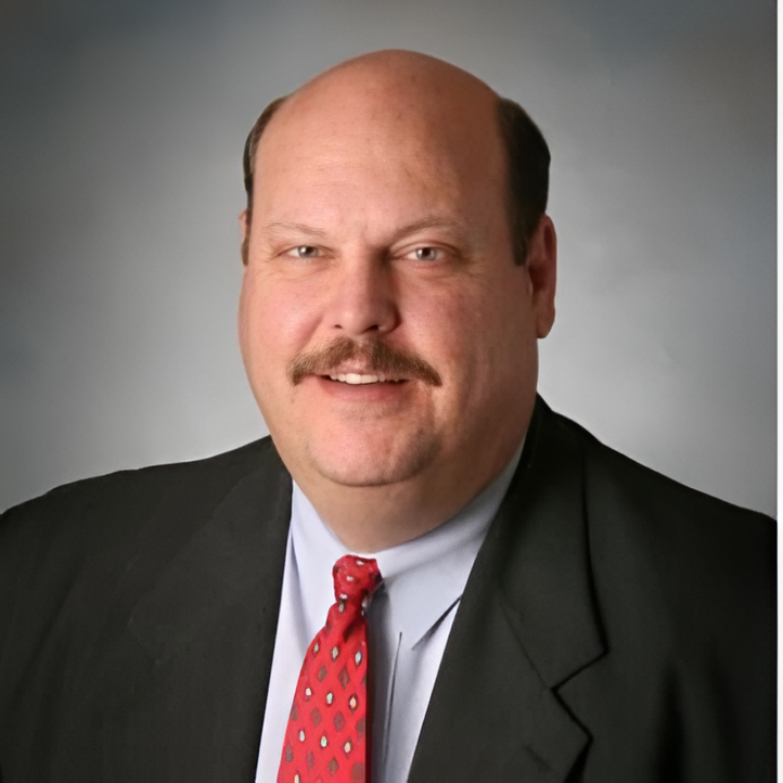 Man in a suit smiles, wearing a red patterned tie; a business portrait.