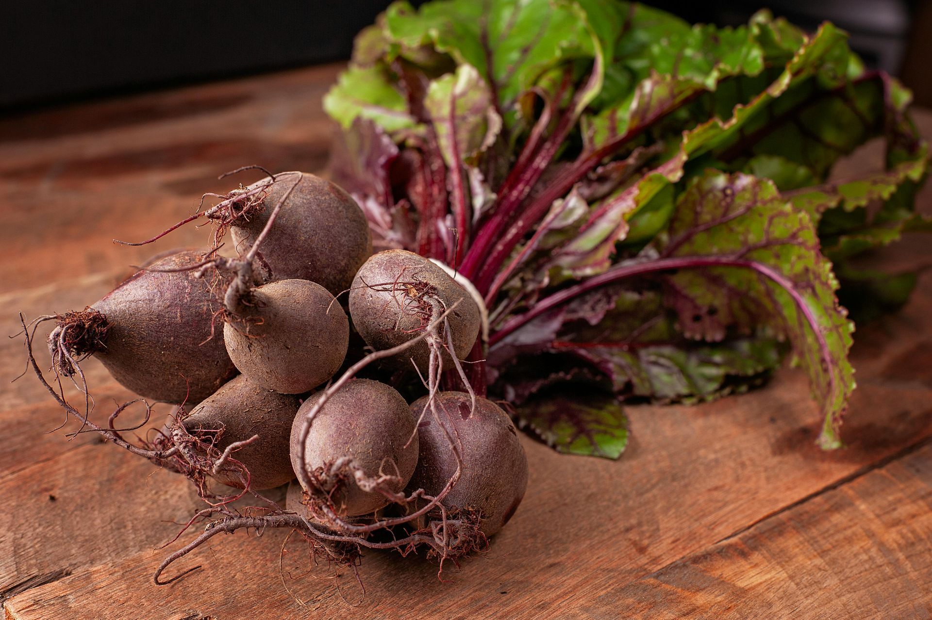 Bunch of freshly harvested beets with green and red leaves on a wooden surface.