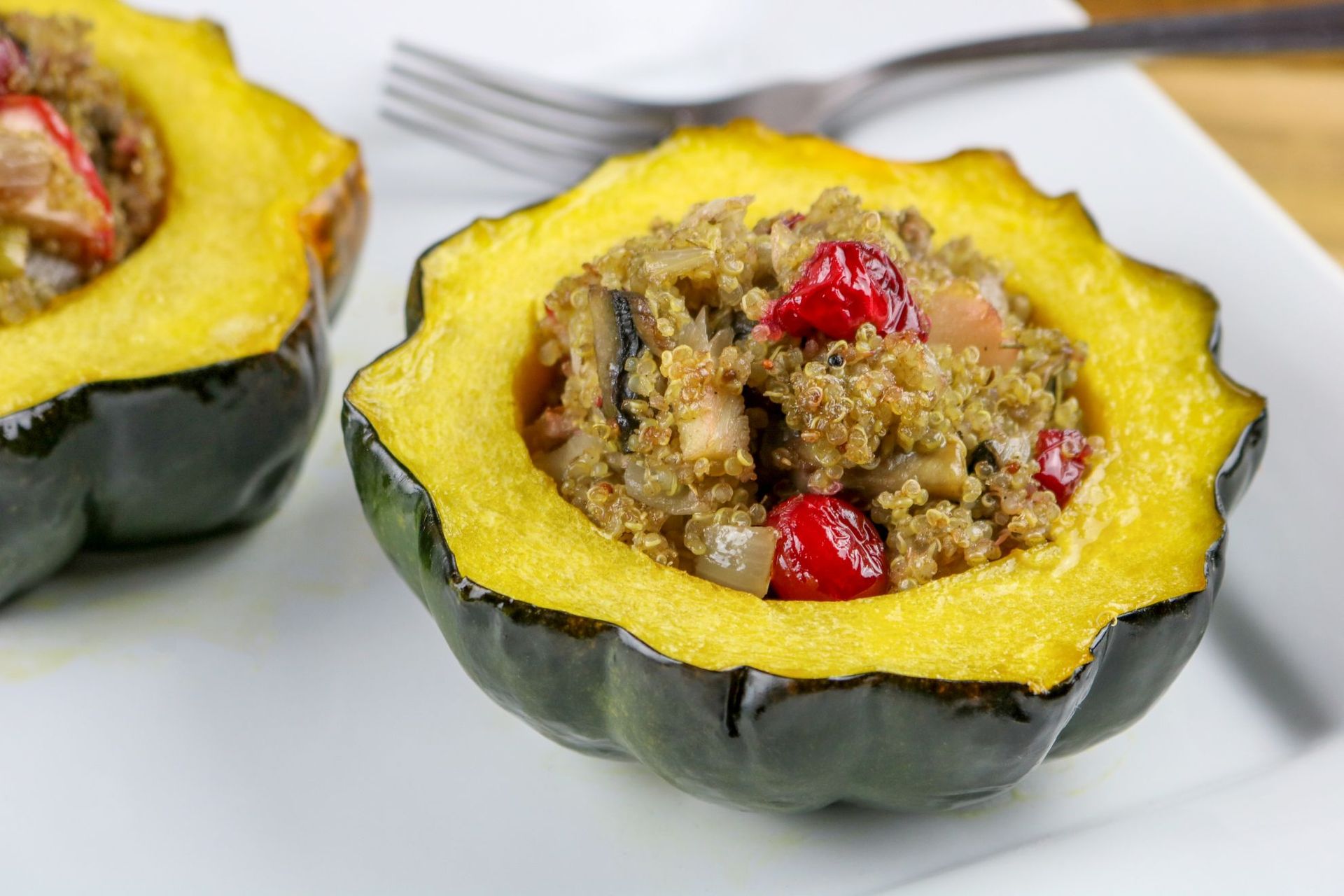 Acorn squash halves filled with quinoa, mushrooms, and cranberries on a white plate.