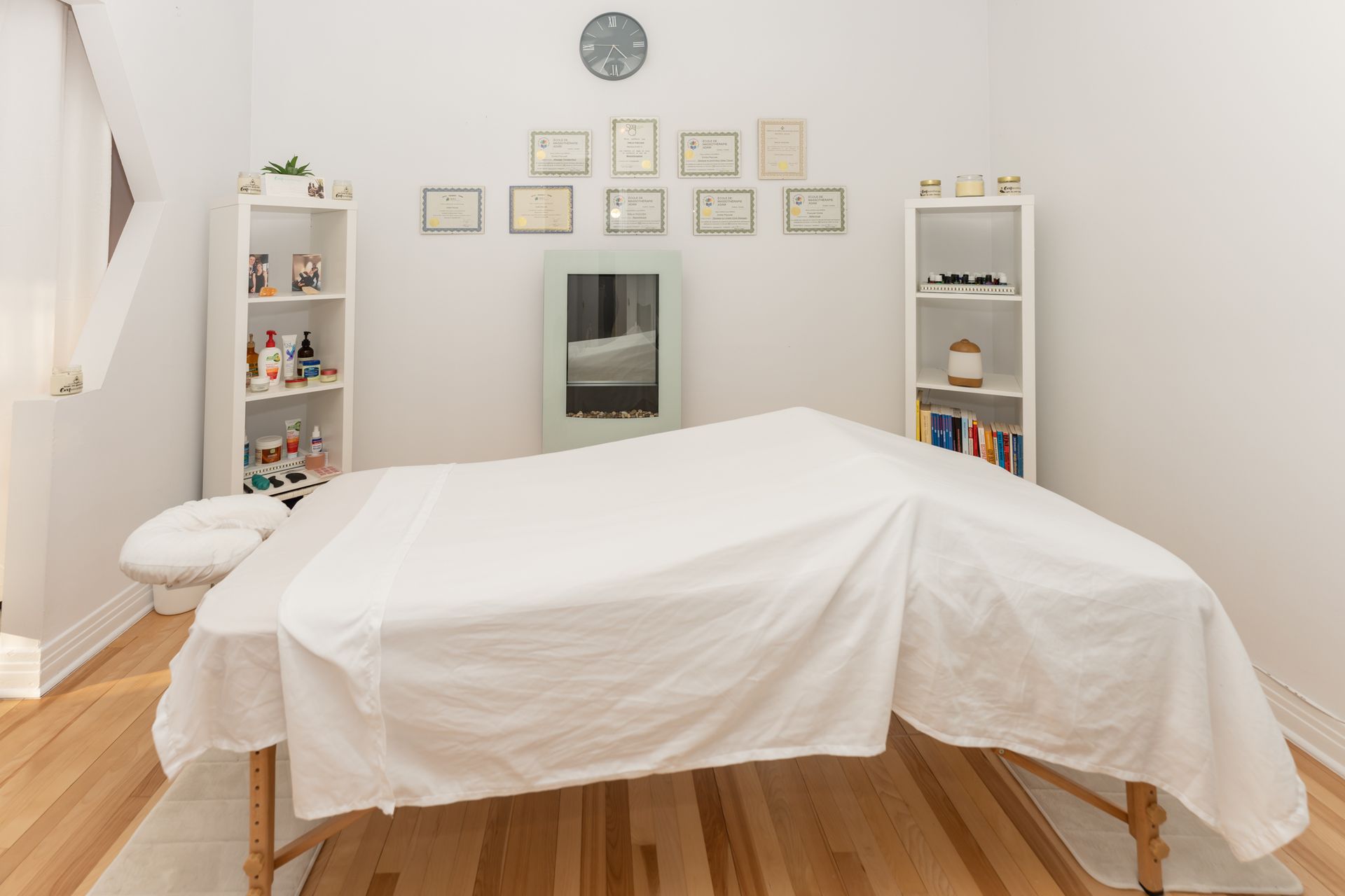 Salle de massothérapie avec table de massage couverte, étagères et certificats encadrés.