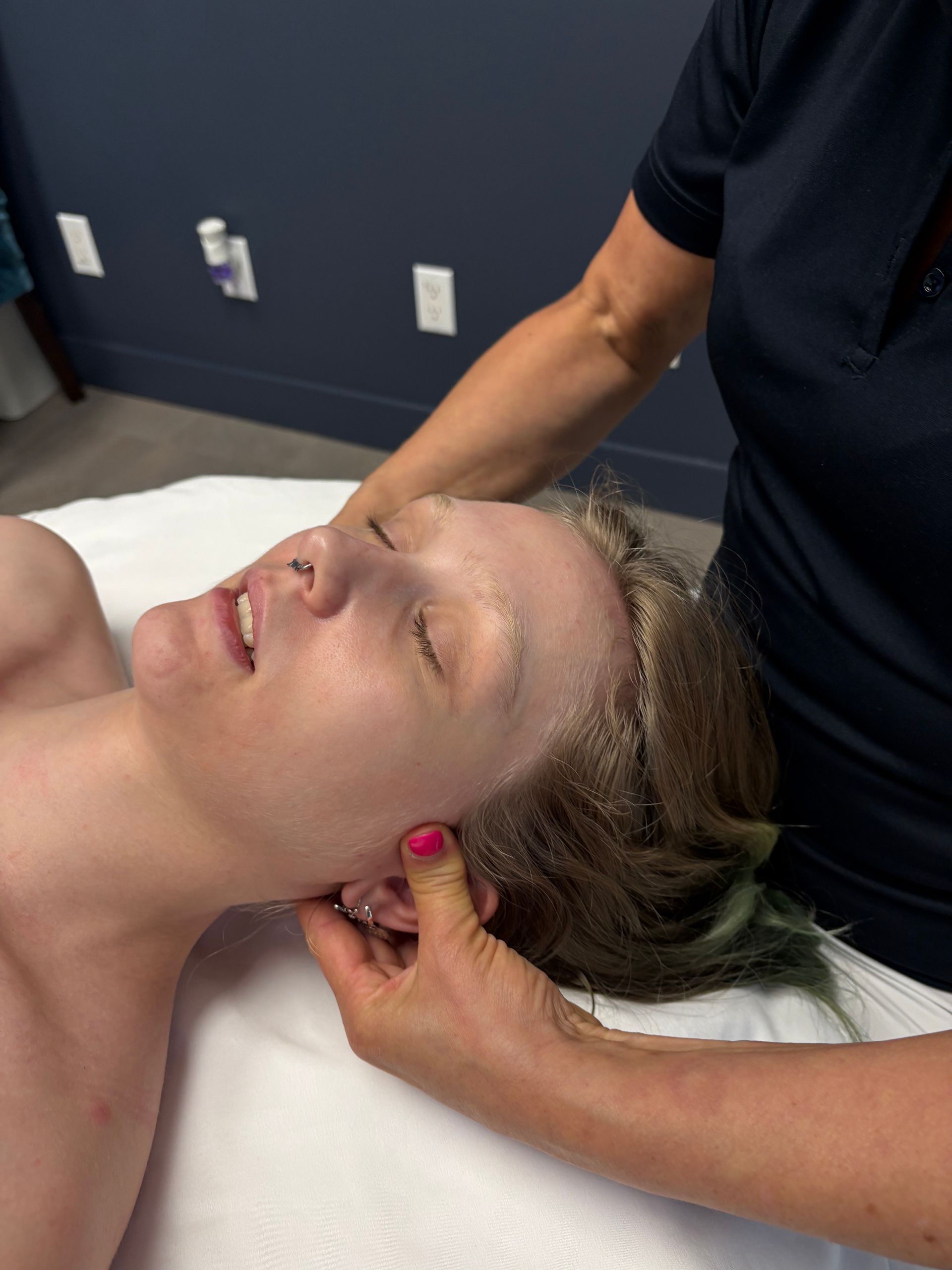 Personne recevant un massage du cou ; mains sur la tête et le cou, visage détendu.