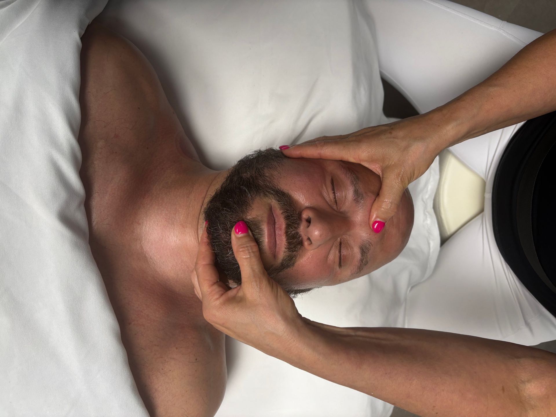 Personne recevant un massage du visage sur une table de massage, les mains sur le visage, les yeux fermés.
