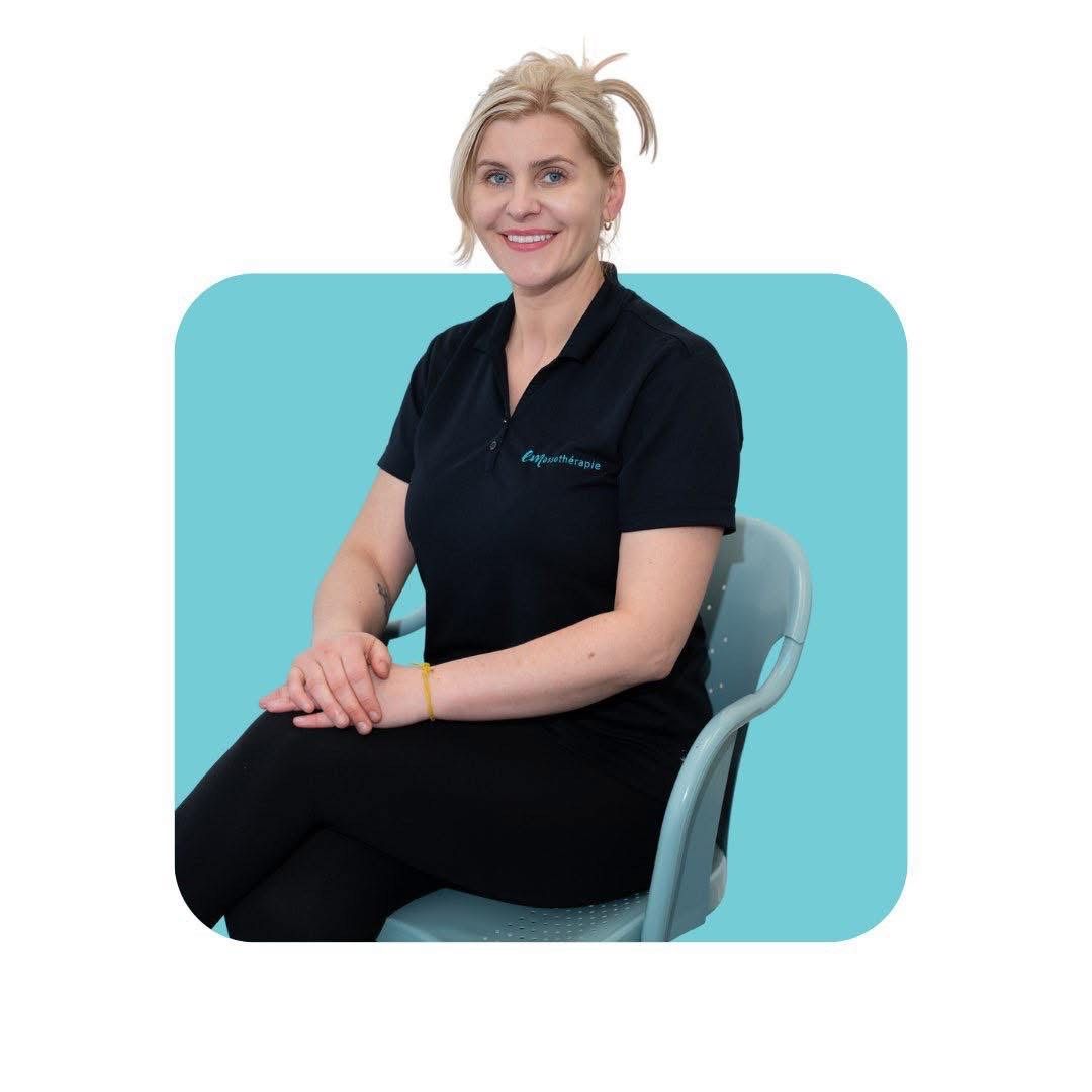 Femme aux cheveux blonds portant une chemise noire et des leggings, assise sur une chaise, souriante.