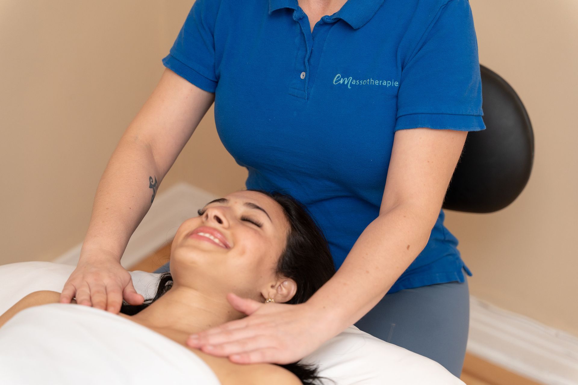 Femme recevant un massage du cou, thérapeute en chemise bleue, souriant, cadre intérieur.