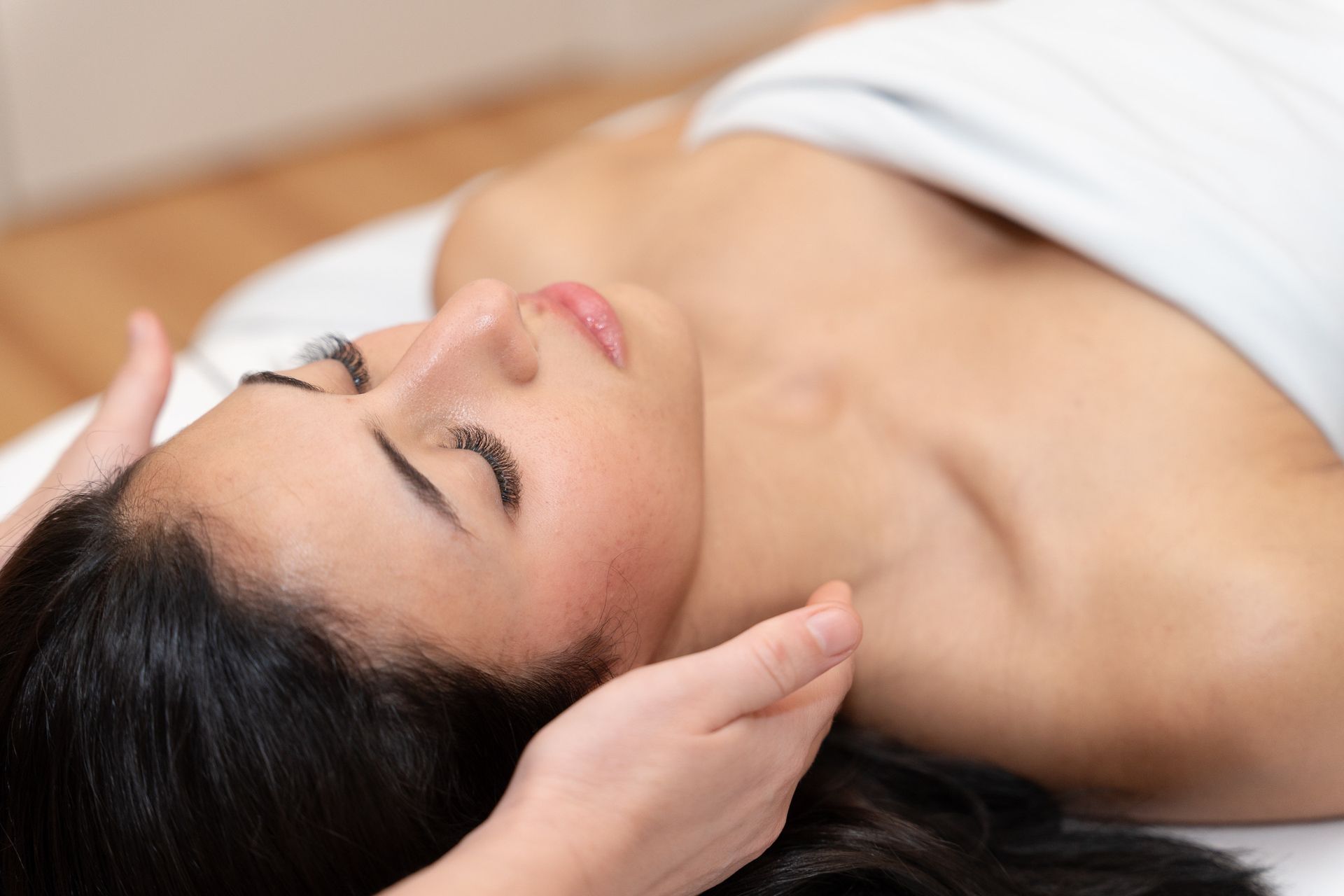 Femme recevant un massage du visage, les yeux fermés, sur une table de massage.