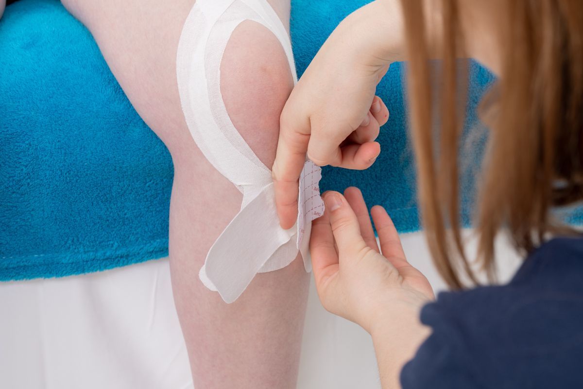 Personne appliquant du ruban adhésif athlétique blanc sur un genou sur une surface bleue.