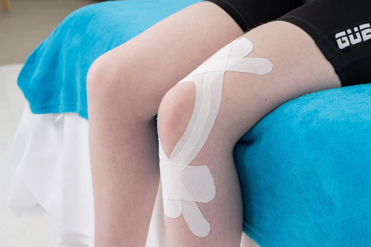 Genou avec du ruban athlétique blanc dessus, plié sur une surface bleue.