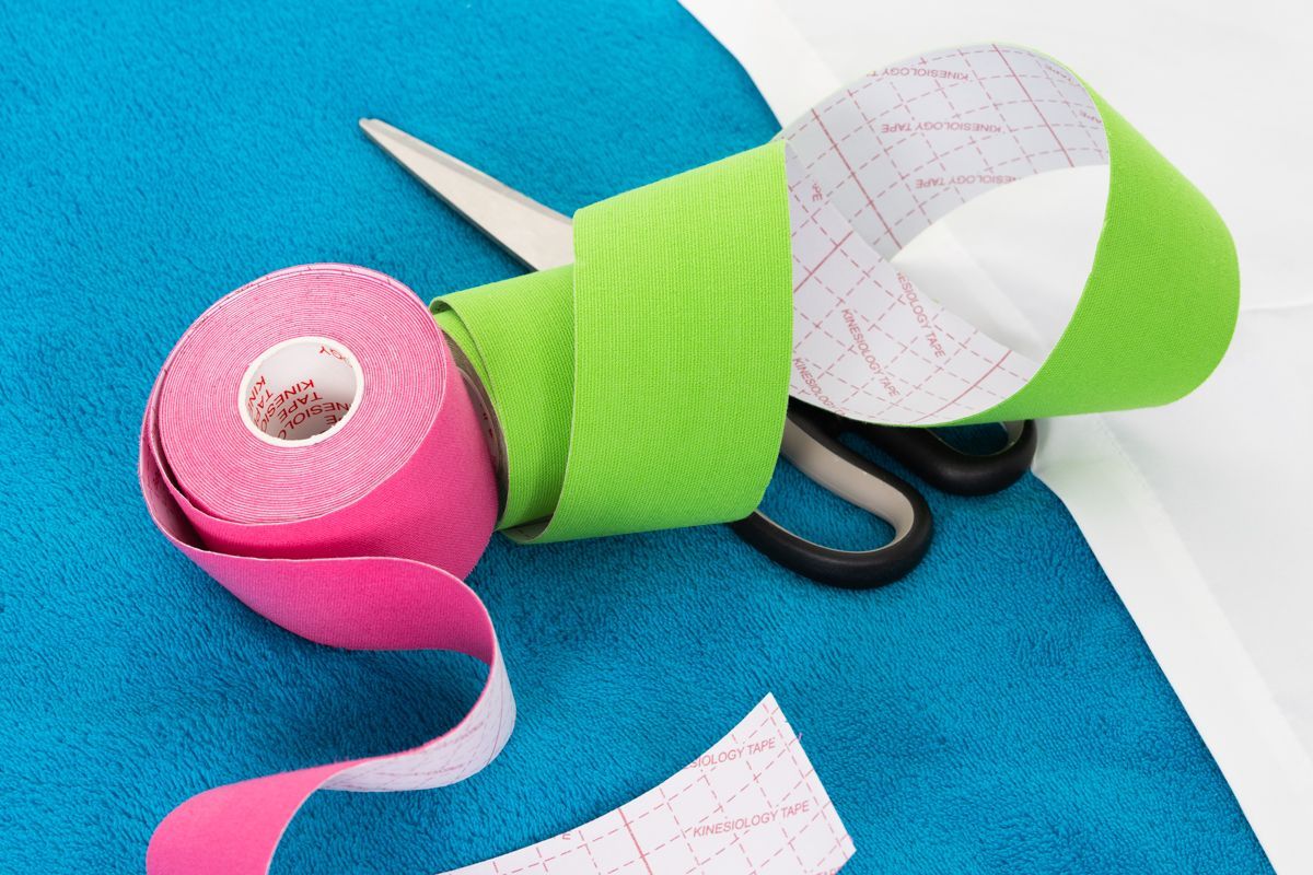 Rouleaux de ruban adhésif athlétique rose et vert avec des ciseaux sur du tissu bleu.