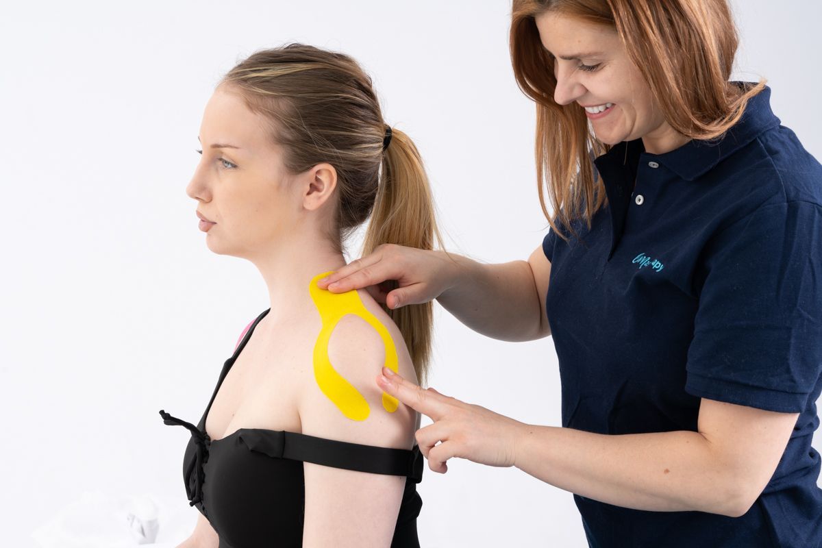 Une femme applique un ruban de kinésiologie jaune sur l'épaule d'un patient. Fond blanc.