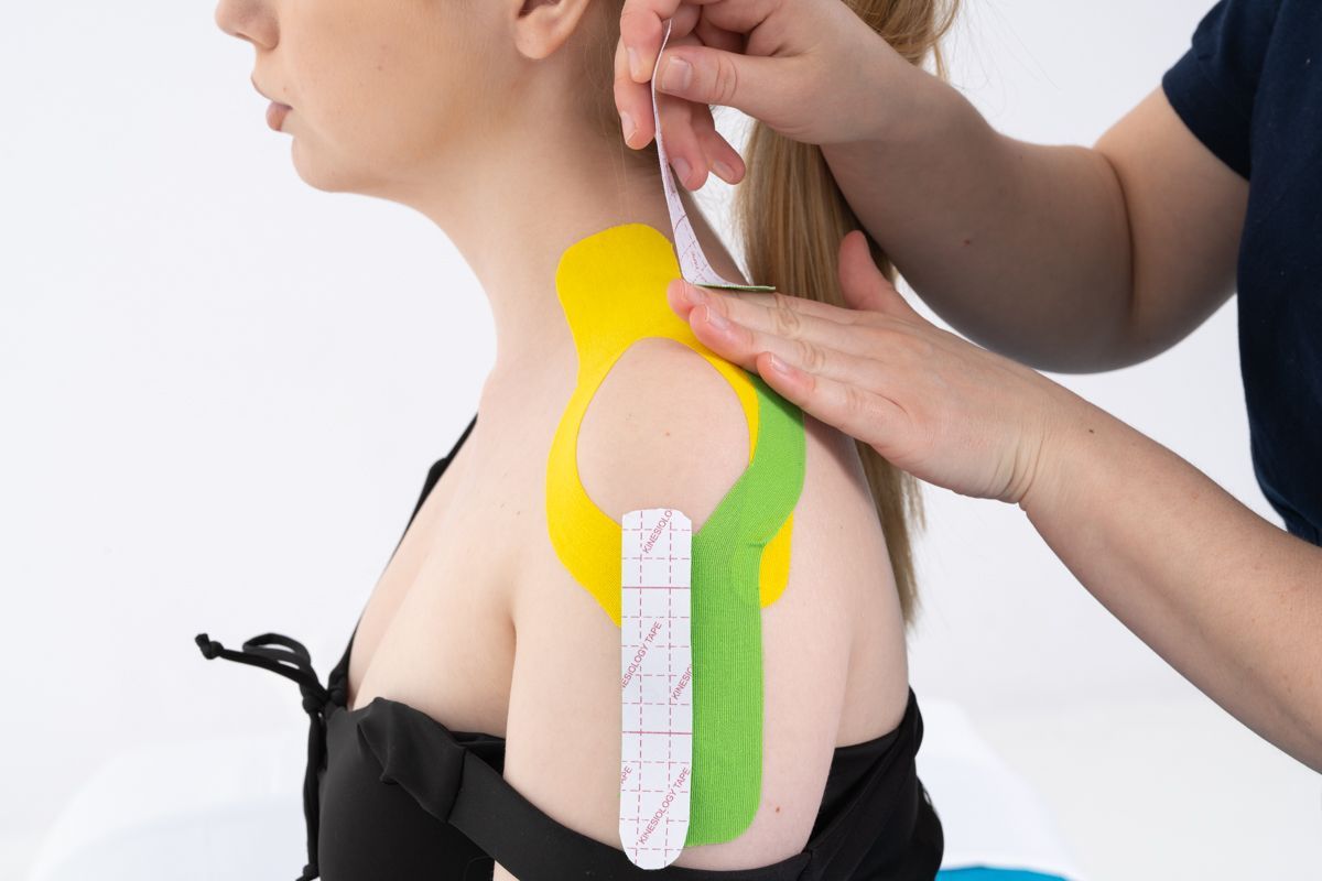 Une personne portant un ruban de kinésiologie jaune et vert sur l'épaule est mesurée par une autre personne.