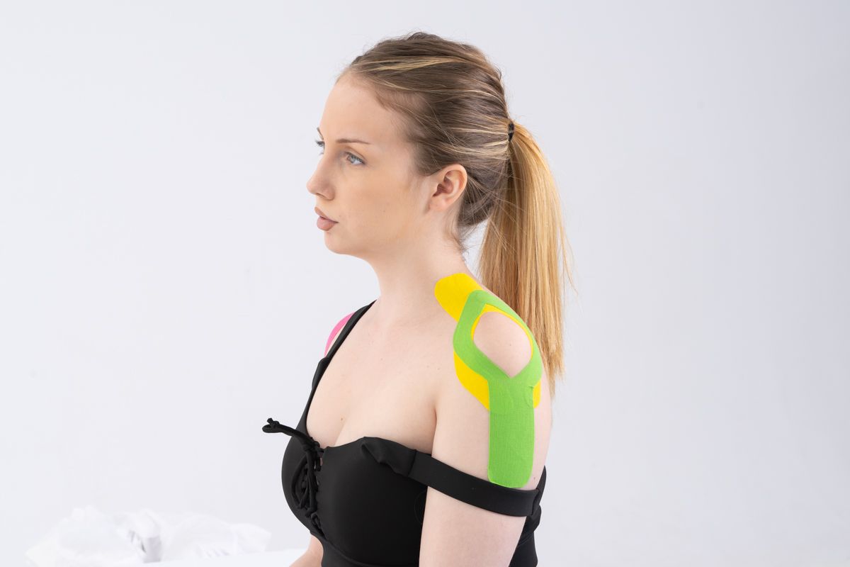 Femme avec du ruban de kinésiologie sur l'épaule, portant un haut noir, profil latéral.