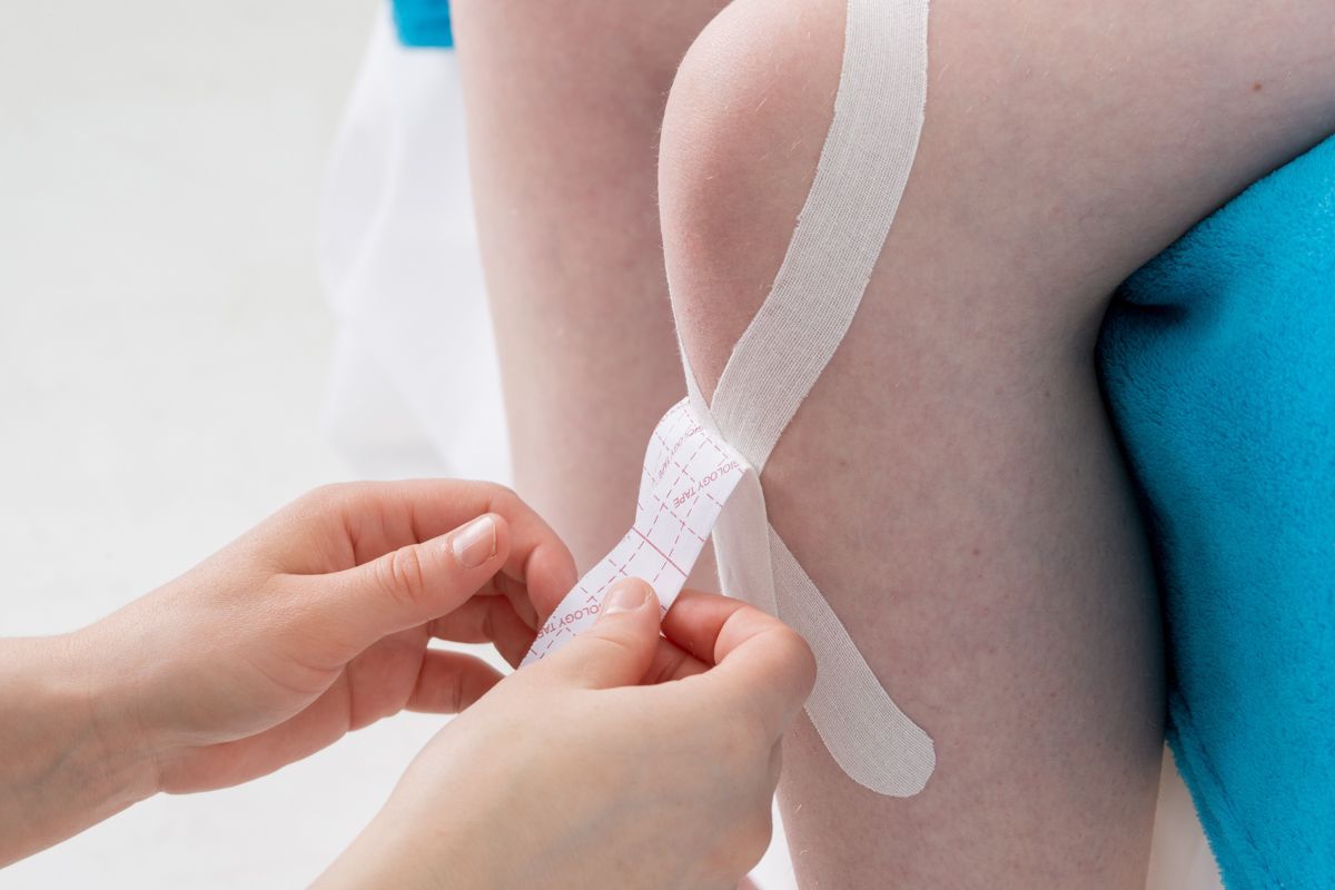 Mains appliquant du ruban kinésiologique sur le genou d'une personne.