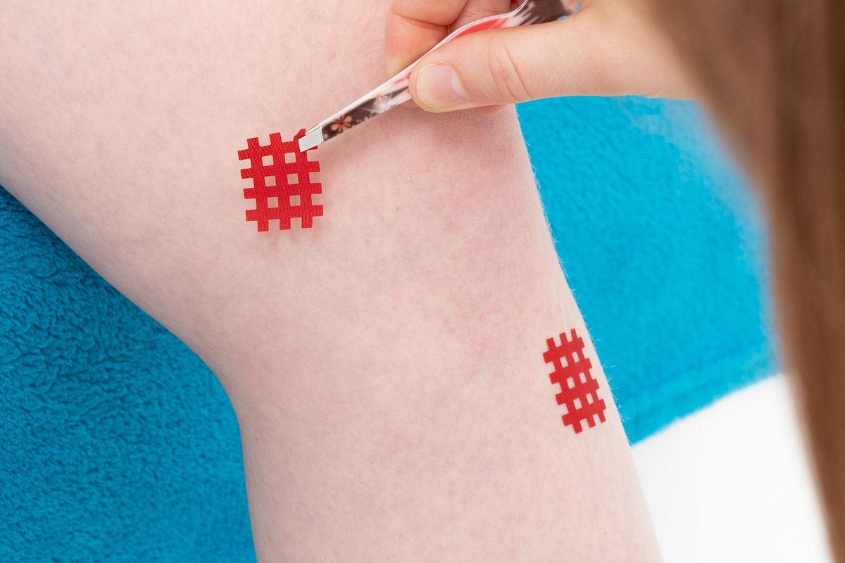 Une personne applique un bandage en maille rouge sur un genou.
