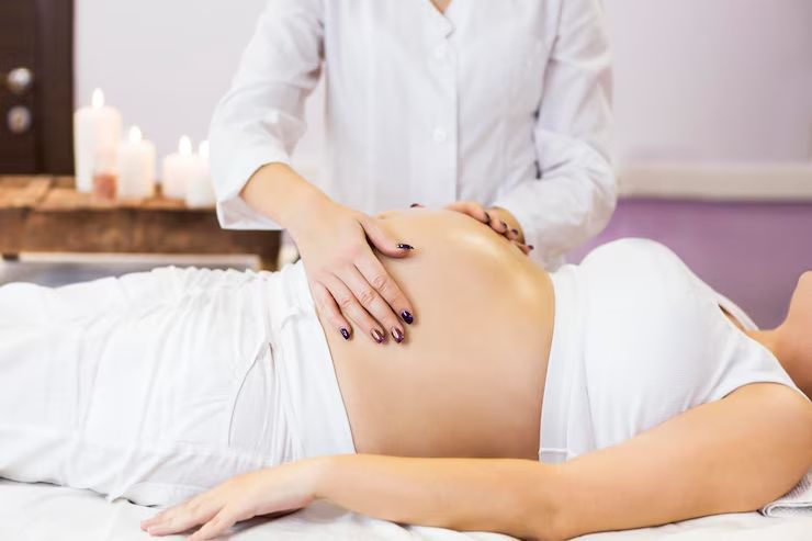 Personne recevant un massage prénatal, mains sur le ventre. Lumière tamisée, bougies.