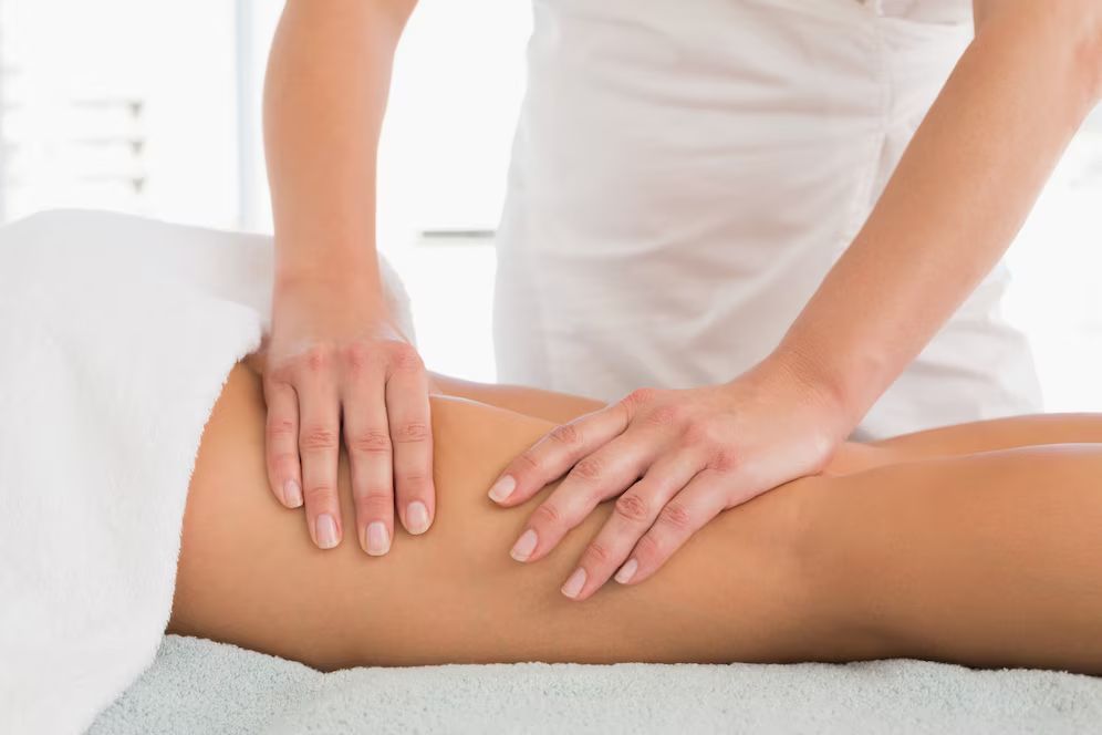 Des mains massent la jambe d'une personne dans un spa ; la personne est sur une table de massage, drapée dans une serviette blanche.