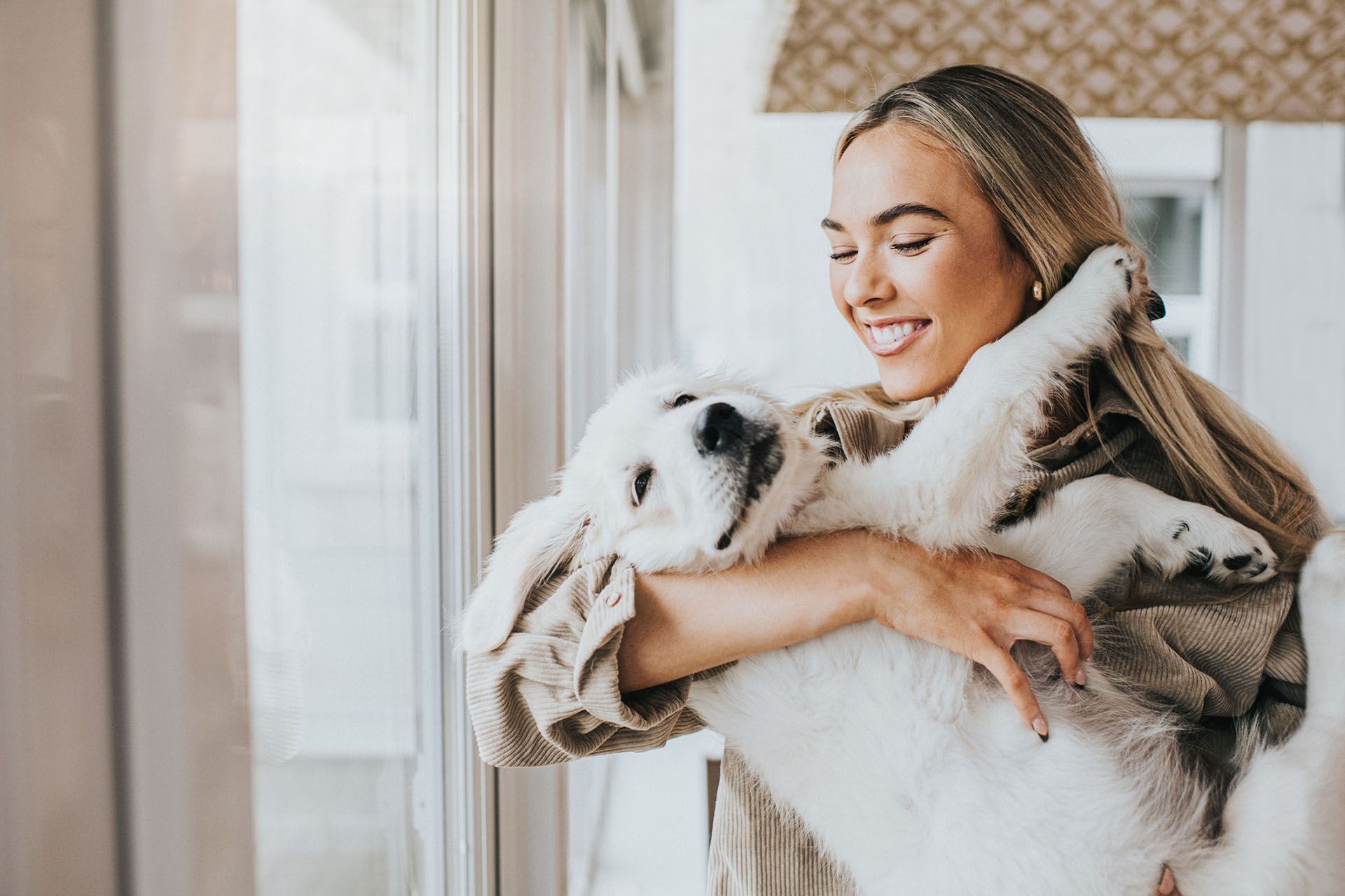A woman is holding a puppy in her arms in front of a window