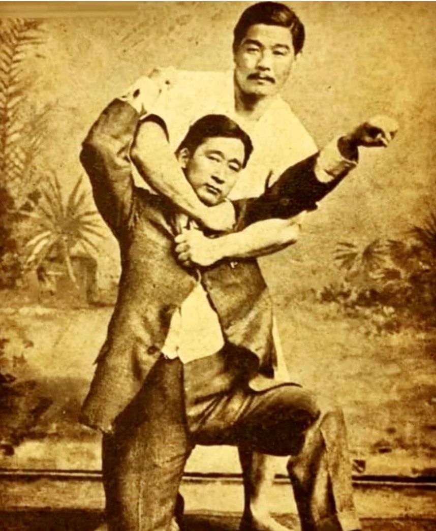 a black and white photo of two men in suits wrestling