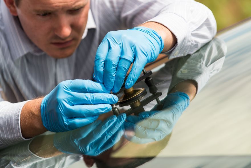 A man is installing a windshield on a car in a garage.