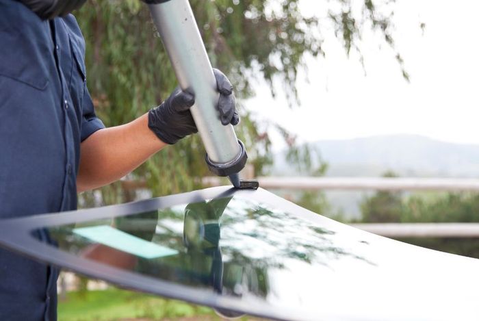 A man is cleaning the windshield of a car in a garage.