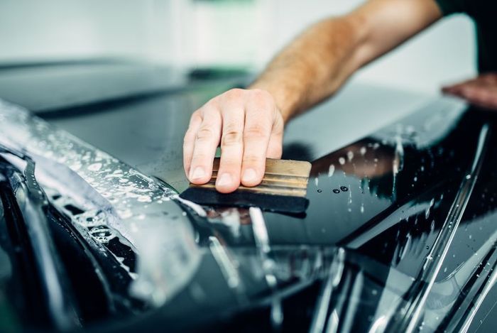 A man and a woman are working on a car windshield in a garage.