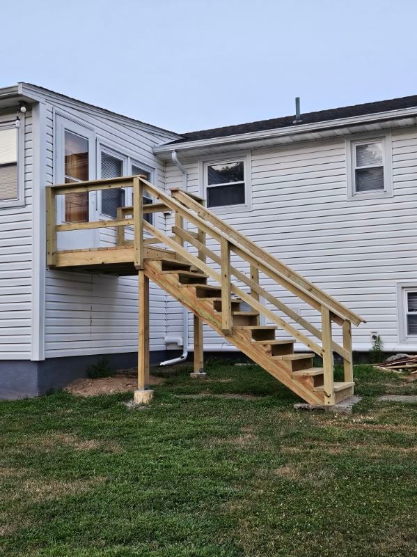 Wooden deck with stairs attached to a white house, on a grassy lawn. The deck has railings.