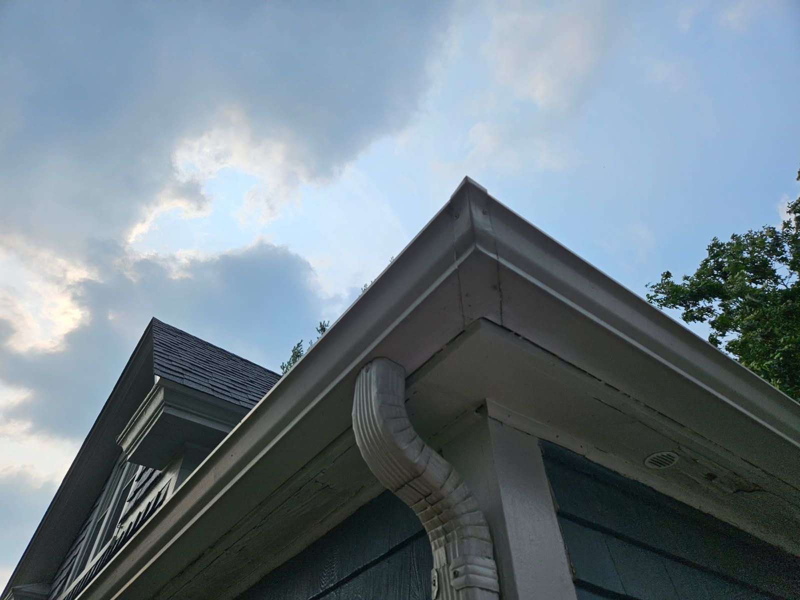 Corner of house with white gutters, downspout, blue siding, and cloudy sky.