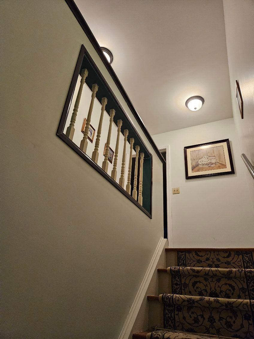 Staircase with floral carpet, light green walls, and framed art. Wooden banister with a dark frame.