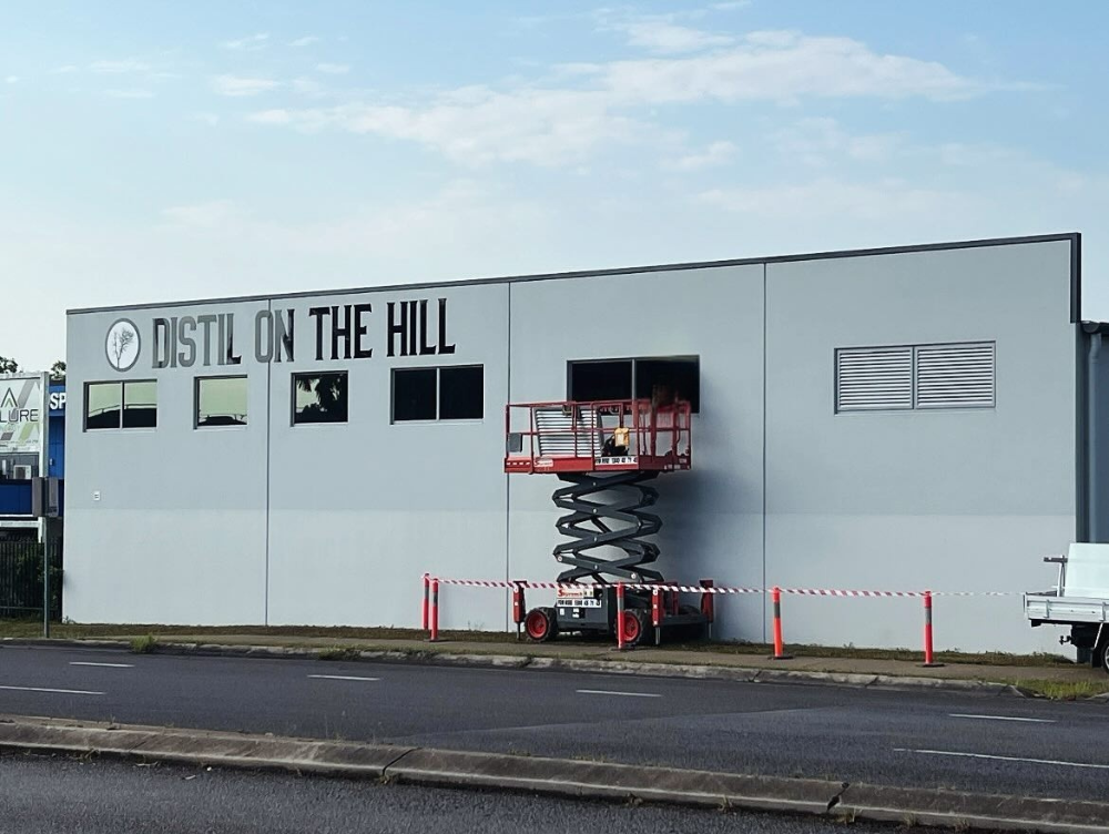 A red scissor lift stands before a grey building labeled — A1 Security Screens Cairns In Manunda, QLD