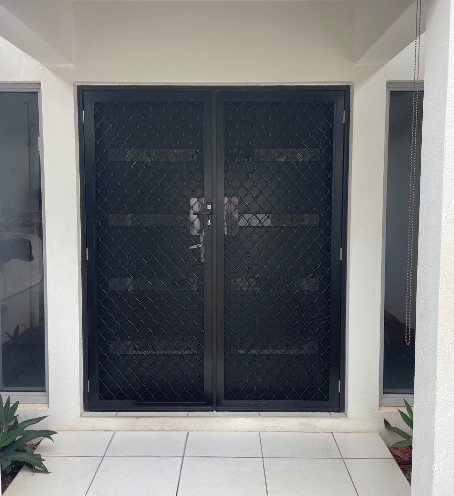 Black security screen double doors on a white building, with windows on either side.— A1 Security Screens Cairns In Manunda, QLD