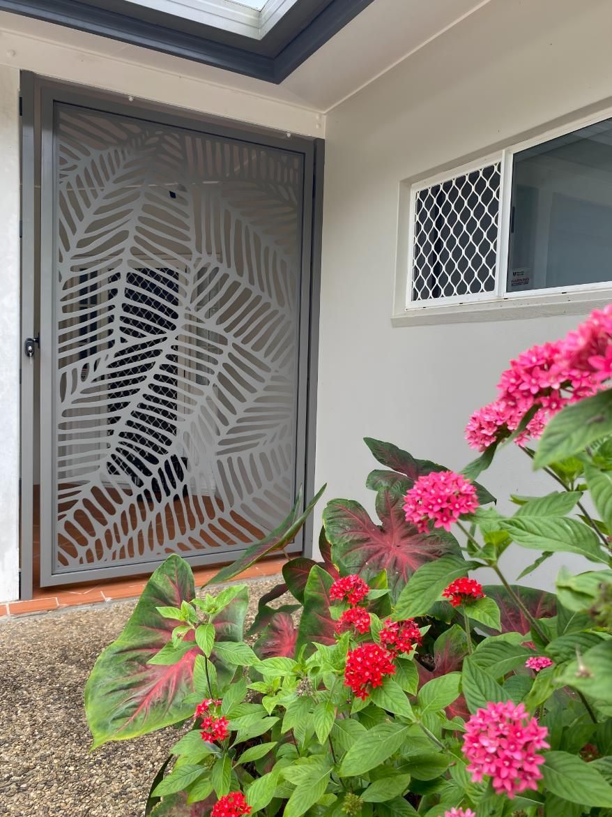 A Door With a Pattern on It is Surrounded by Pink Flowers — A1 Security Screens Cairns In Manunda, QLD