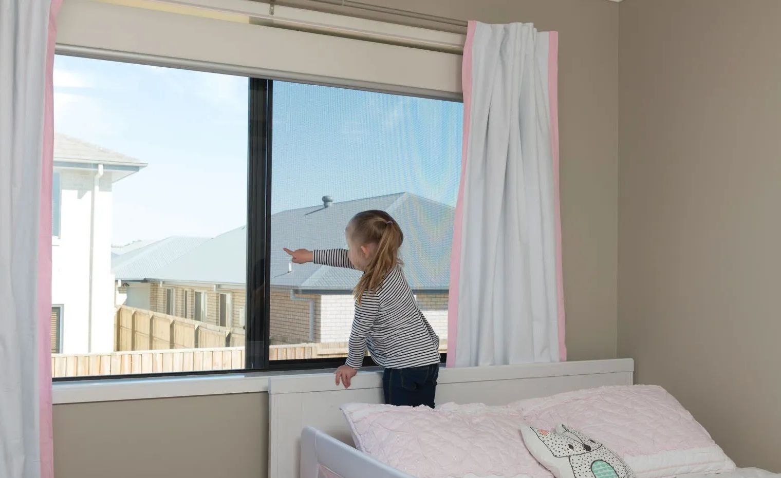 A Little Girl is Standing in Front of a Window in a Bedroom — A1 Security Screens Cairns In Manunda, QLD