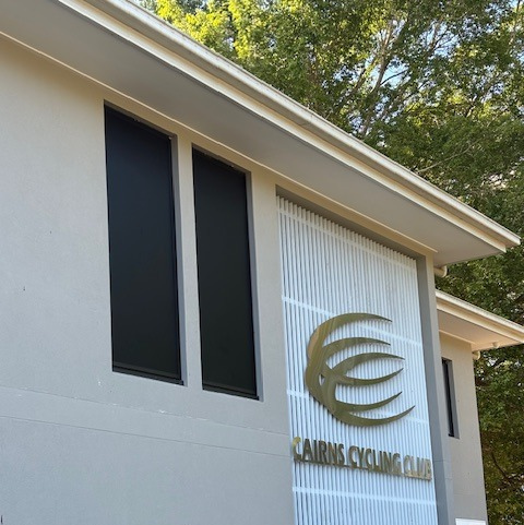 Cairns Cycling Club building exterior, gray walls, black windows, gold logo, white decorative panel.