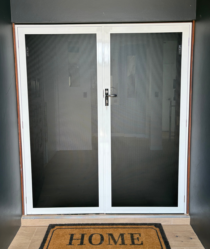 White-framed double screen door with black screen, brown doormat that reads