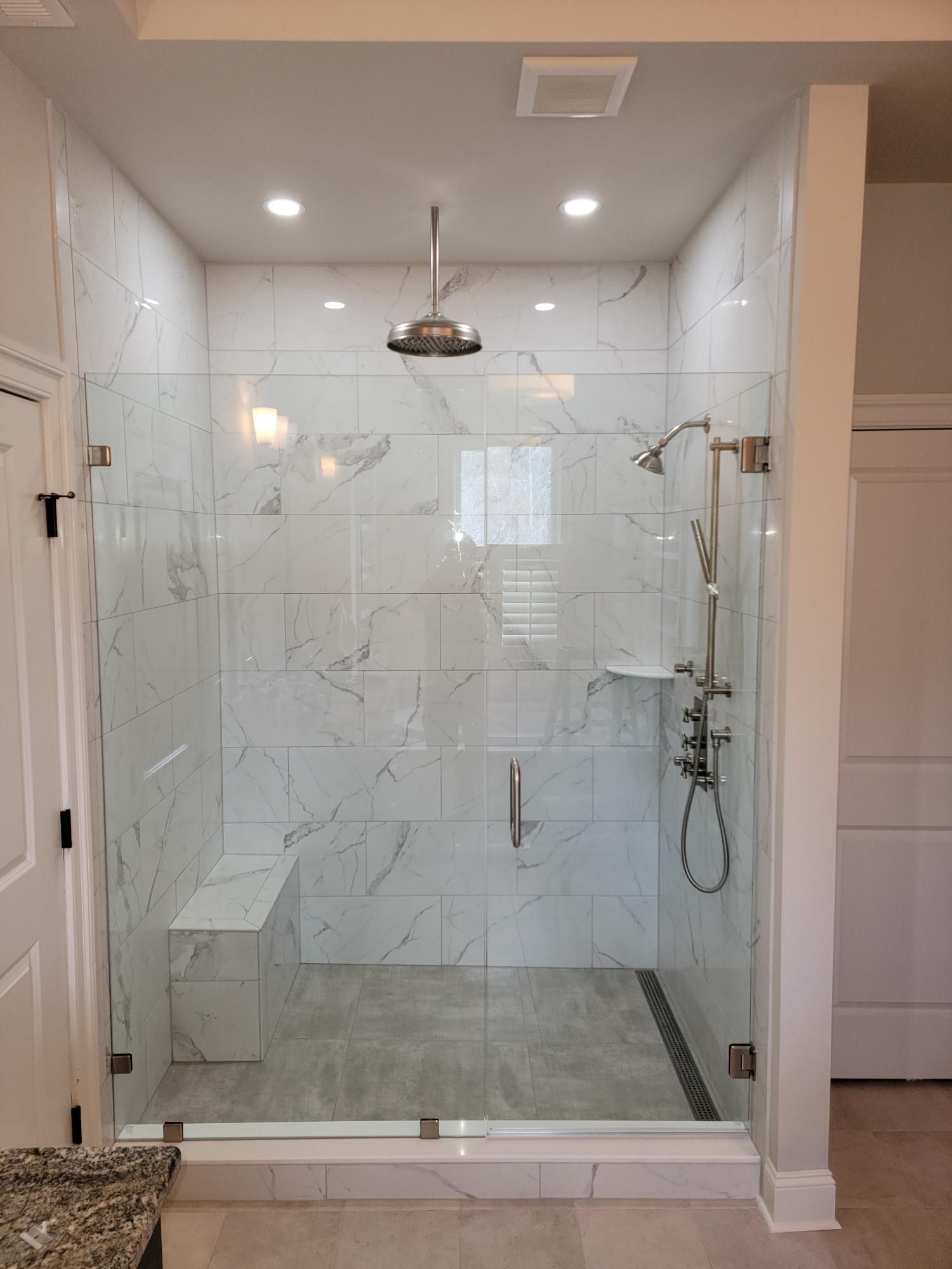 Walk-in shower with glass enclosure, white marble tiles, rain showerhead, and chrome fixtures